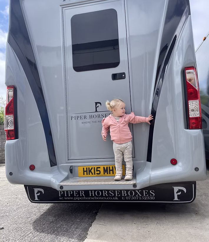 Small girl standing on back on horsebox